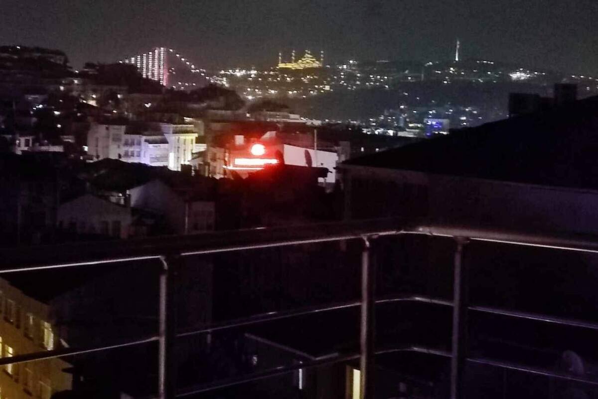 A nighttime cityscape with buildings and a prominent hill with lights.