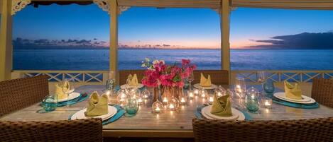 A table set for dining with a view of the sea at dusk.