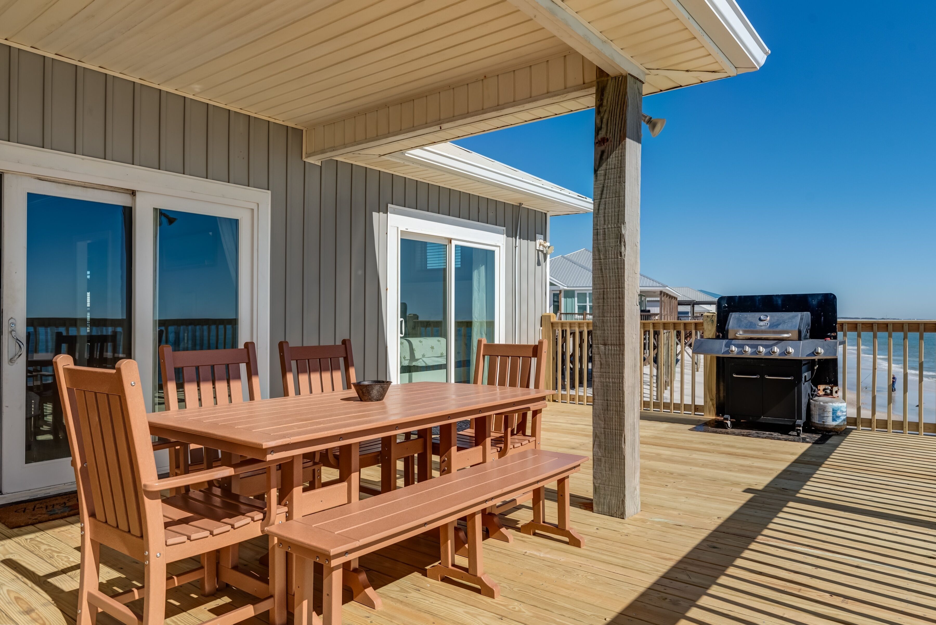 Un patio in legno con tavolo e sedie, un barbecue e vista sulla spiaggia.