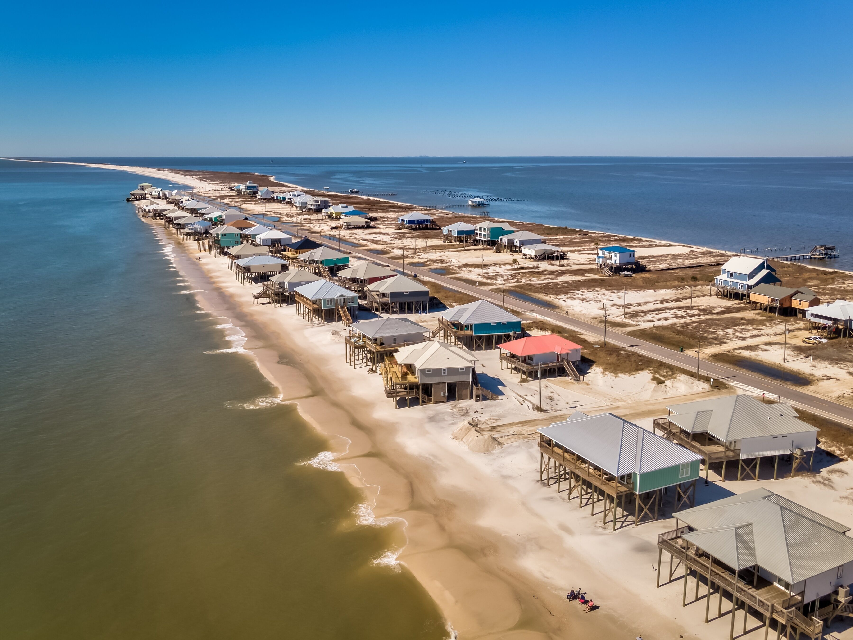 An aerial view of a coastal area with multiple beach houses connected by walkways to the beach.