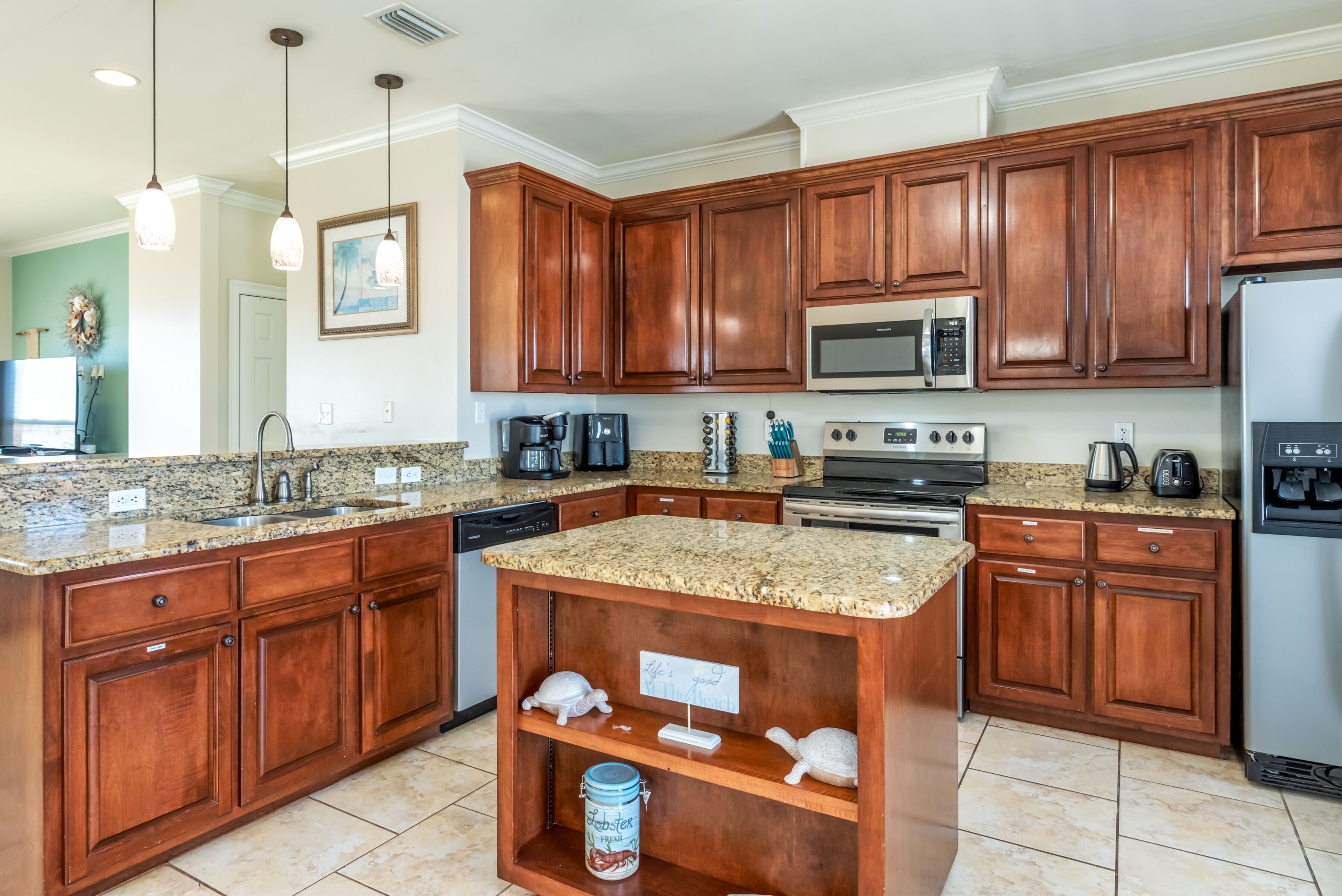 A kitchen with granite countertops, wooden cabinets, stainless steel appliances, and a small island with a sign.