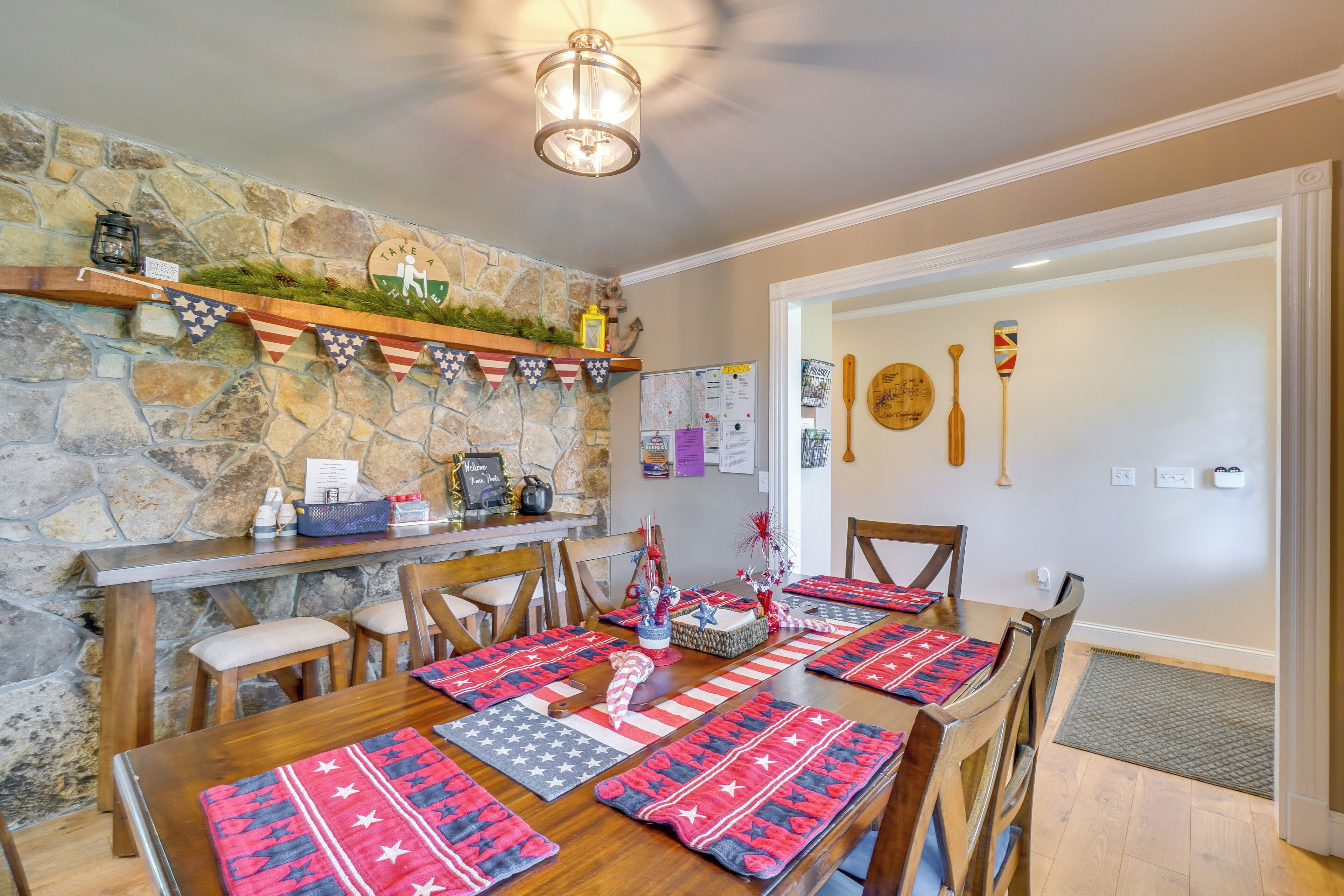 Un comedor con pared de piedra, mesa y sillas de madera. Hay protectores de mesa con un estampado de estrella, un estante con adornos y un farol en la pared.