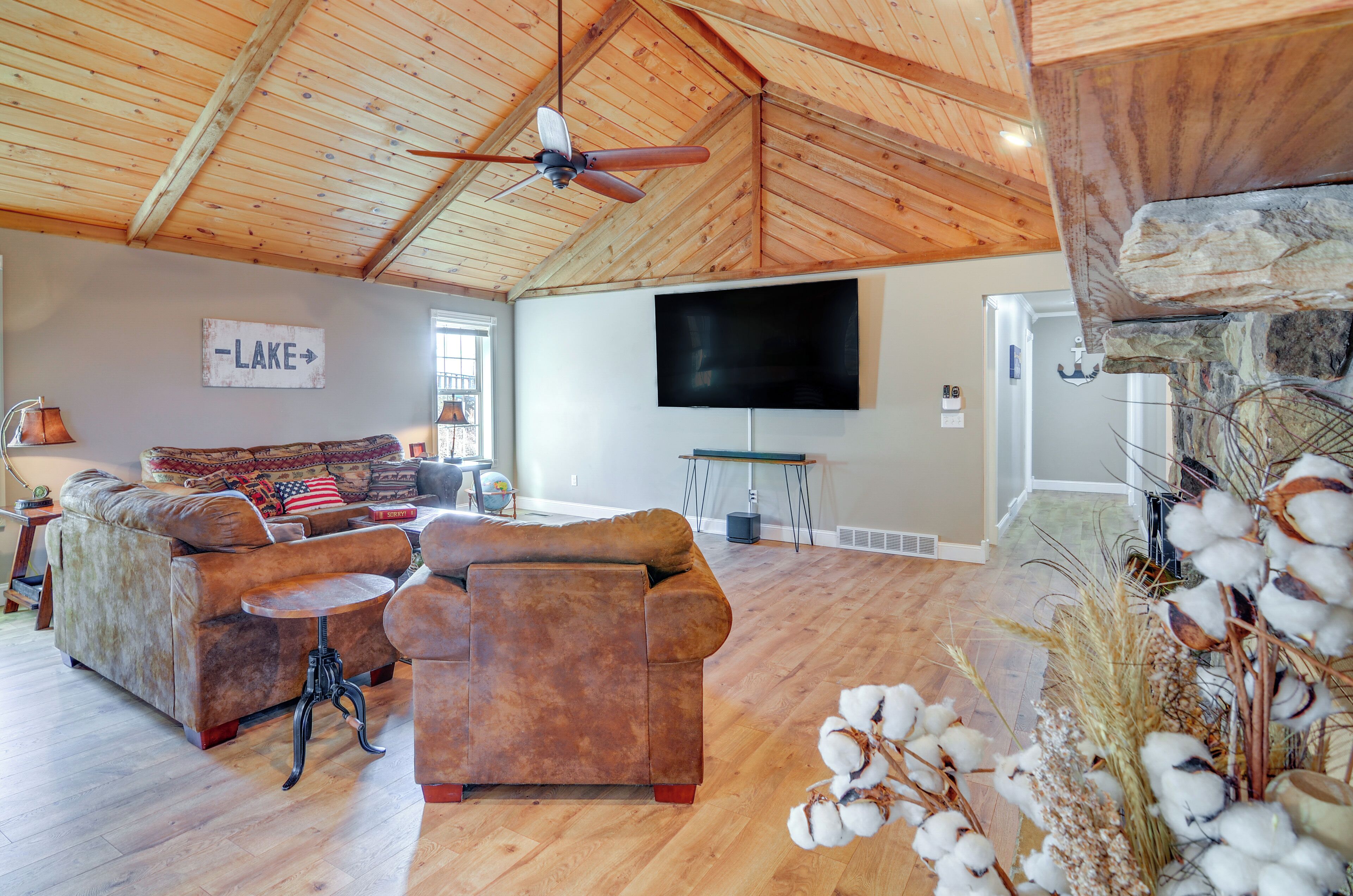 A spacious living room with a high ceiling, a large flat-screen TV, a leather sofa, and a stone fireplace.