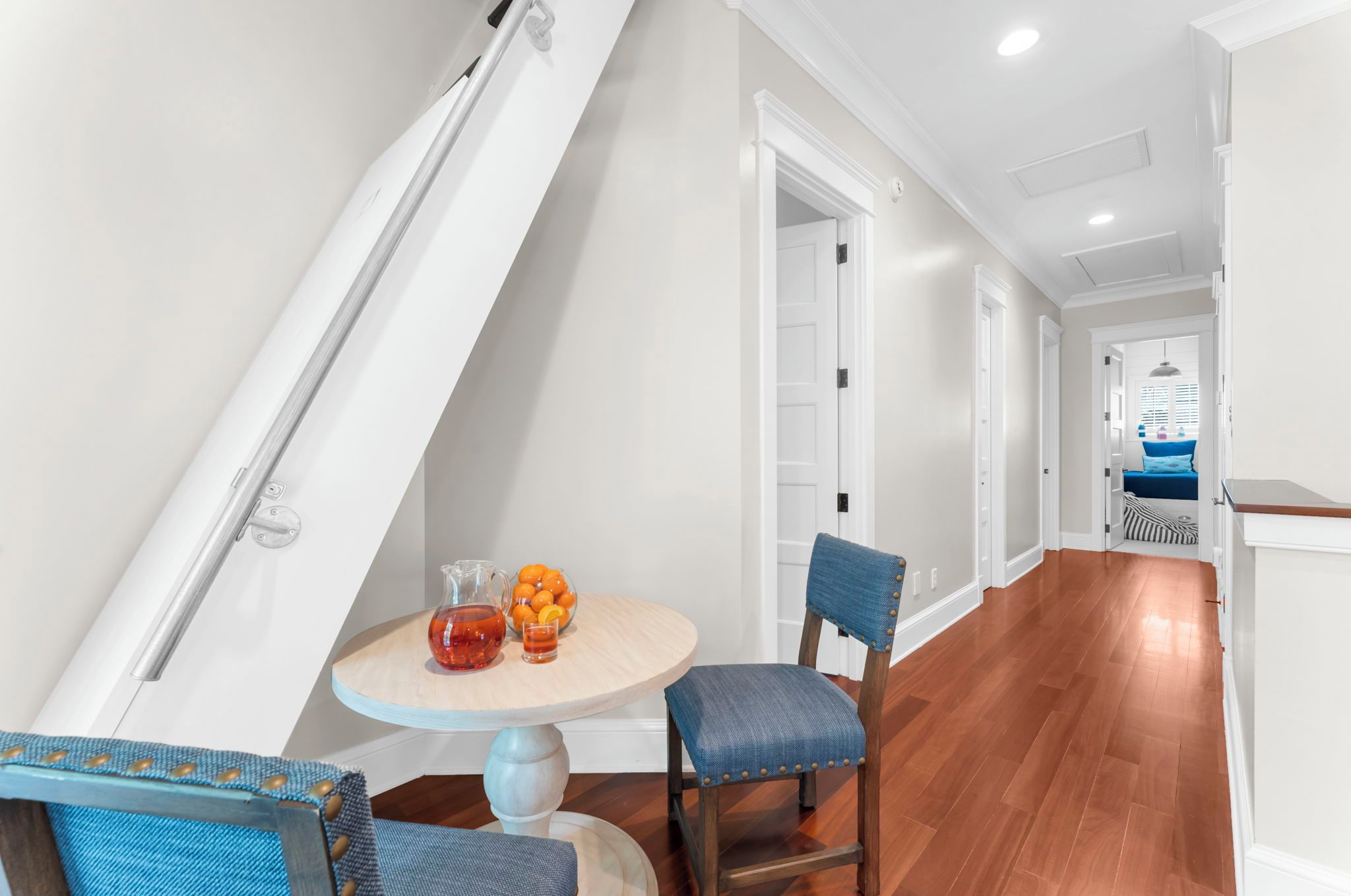 A modern interior with a staircase, a round table with chairs, and a view into another room with a blue sofa.