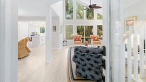 Ein geräumiger Wohnbereich mit hohen Decken, einem Deckenventilator und großen Fenstern mit Blick ins Freie.