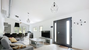 A modern living room with a grey sofa, a coffee table, a TV, and a dining area with chairs and a table. - Villa 2 Chambres Avec Jacuzzi (Bonifacio)