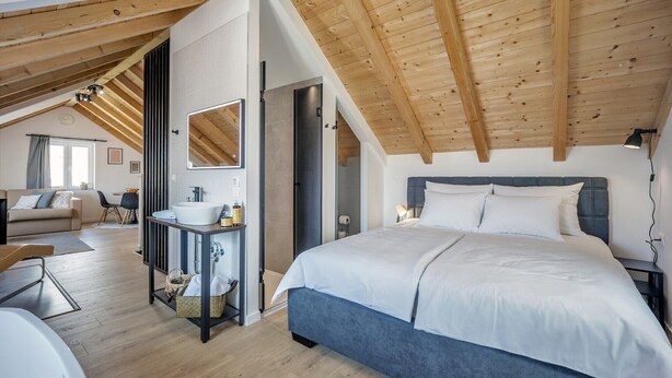 A bedroom with a large bed, wooden ceiling beams, a bathroom with a sink and mirror, and a living area with a sofa and chairs. - Rooftop Studio apartment Yucca for 2+2, 2-min to the beach and 5 to Trogir (Trogir)