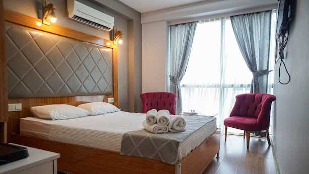 A hotel room with a bed, a chair, a desk, and a window with curtains. - Gama Residence (Izmir)