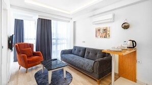 A modern living room with a sofa, armchair, coffee table, and a small wooden side table with a kettle. - Gama Residence (Izmir)