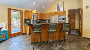 A kitchen with wooden cabinets, a stainless steel refrigerator, a microwave, and a bar area with stools.