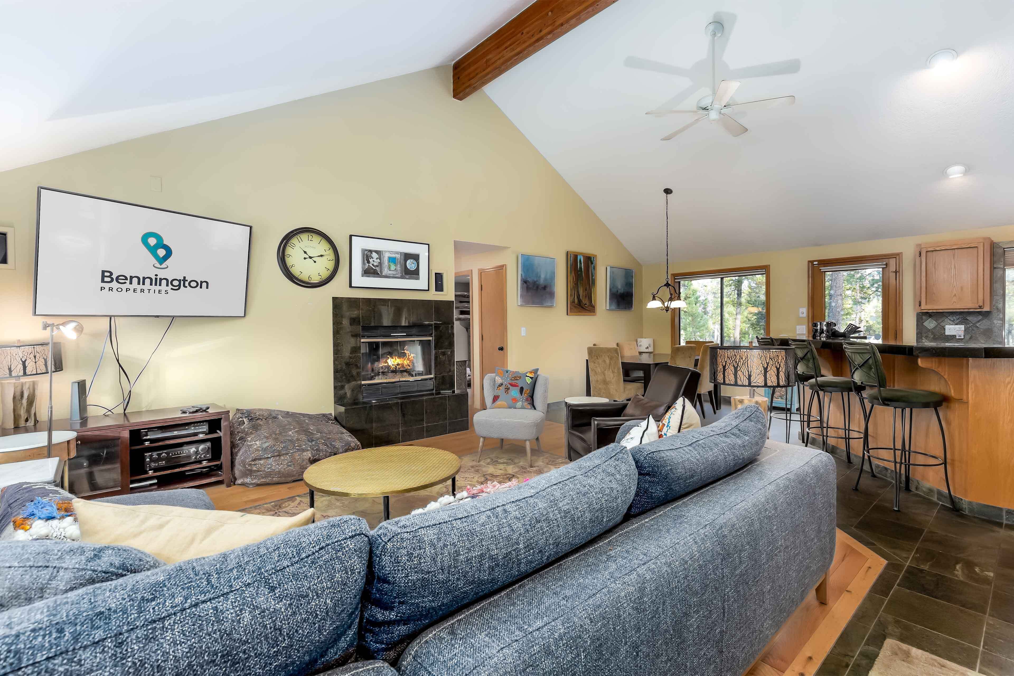 A spacious living room with a large gray sectional sofa, a fireplace, a flat-screen TV, and a dining area with bar stools.