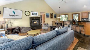 A spacious living room with a large gray sectional sofa, a fireplace, a flat-screen TV, and a dining area with bar stools.