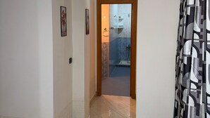Un couloir agrémenté d’un luminaire moderne, une porte donnant accès à une salle de bain et un rideau à motifs.