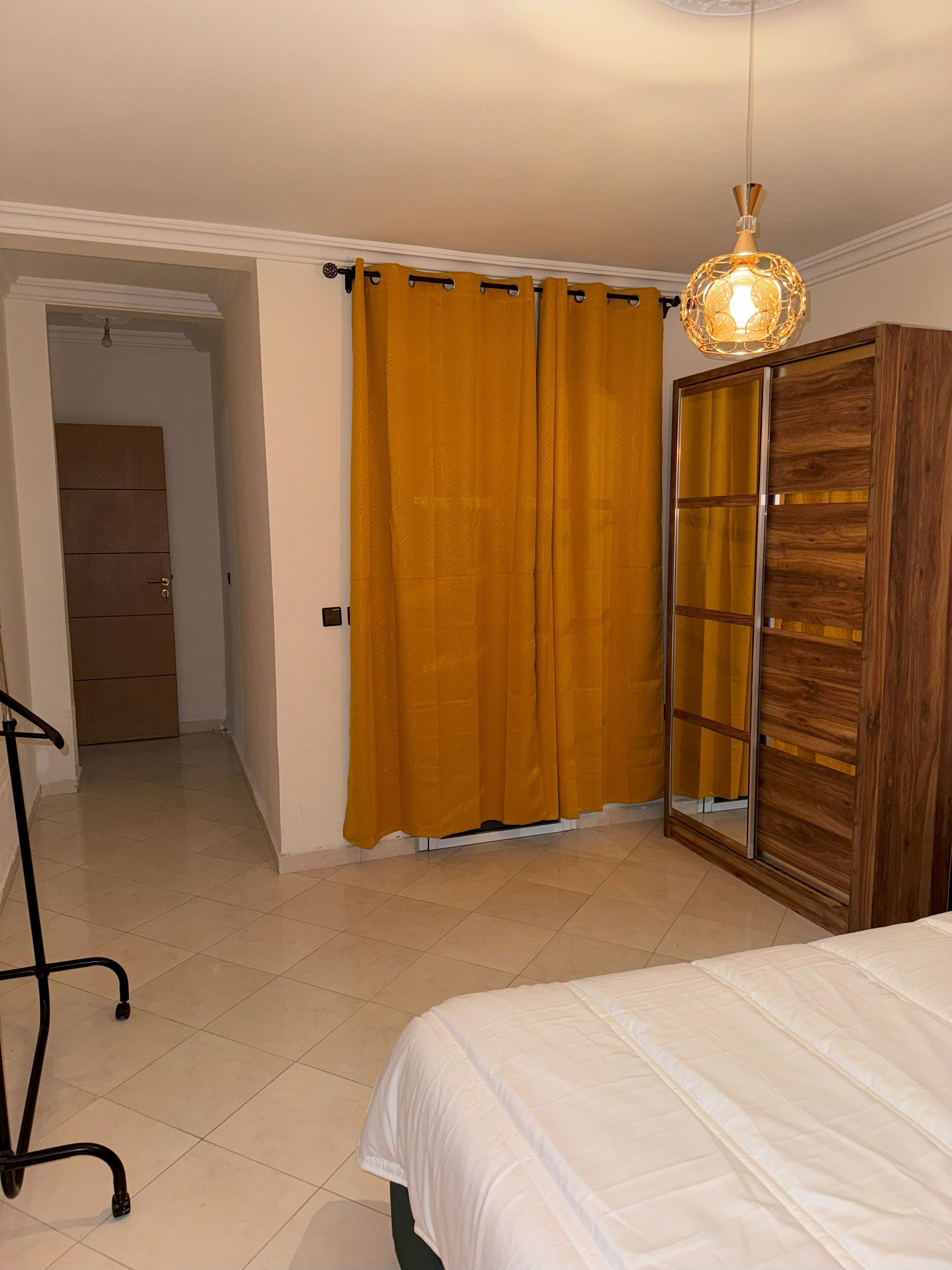 Ein Schlafzimmer mit einem Bett, einem Kleiderschrank, einem Vorhang und einer Pendelleuchte.