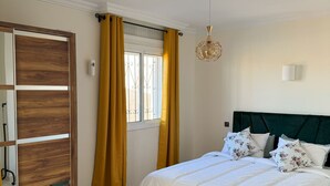 Une chambre à coucher avec un lit, une armoire, une fenêtre avec des rideaux et un luminaire au plafond.