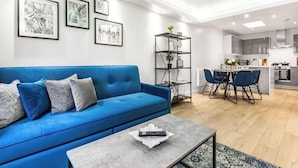 A modern living room with a blue sofa, a coffee table, and a dining area with a kitchen in the background. - Premium Central Apartment | Free Parking | WiFi (Hampshire)