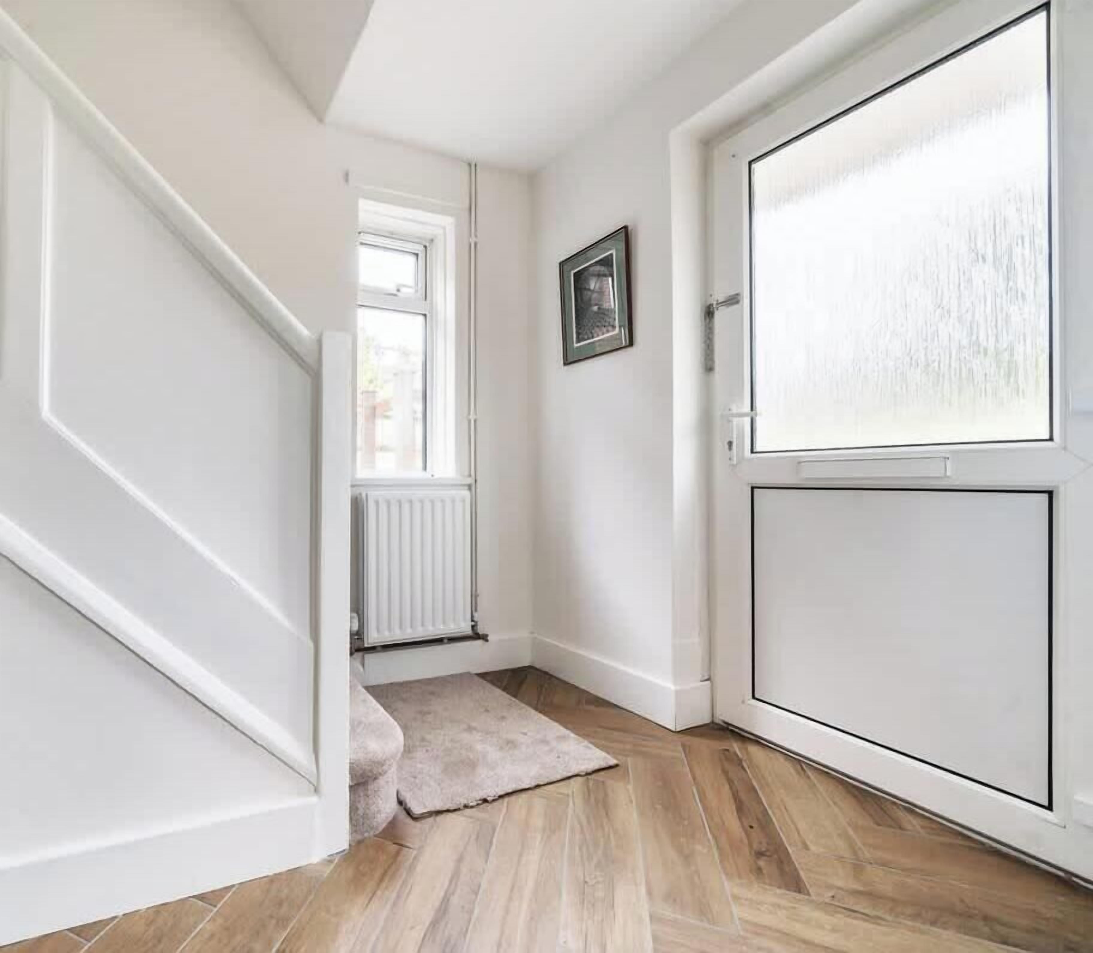 Un couloir avec une porte blanche, un radiateur et une fenêtre.