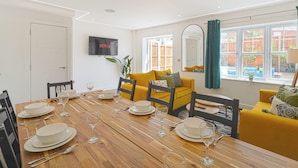 A dining area with a wooden table set for six, a yellow sofa, and a TV mounted on the wall. - Huge House, Contractors/Families, 2X Free Parking (Hampshire)