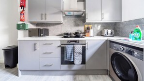 A compact kitchen with a dishwasher, washing machine, and a microwave. There are cabinets, a toaster, and a fire extinguisher visible.