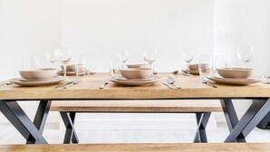 A dining table set with plates, bowls, and cutlery, with a bench in front.