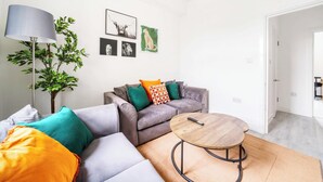 A modern living room with a grey sofa, colorful cushions, a round wooden coffee table, and a floor lamp.