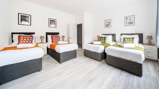 A hotel room with two single beds, a double bed, and a small desk with a lamp.