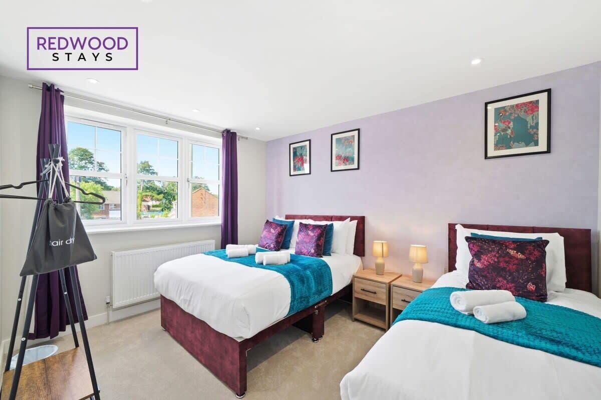 Una habitación de hotel con dos camas, una ventana con cortinas, una lámpara de pie y obras de arte en las paredes.