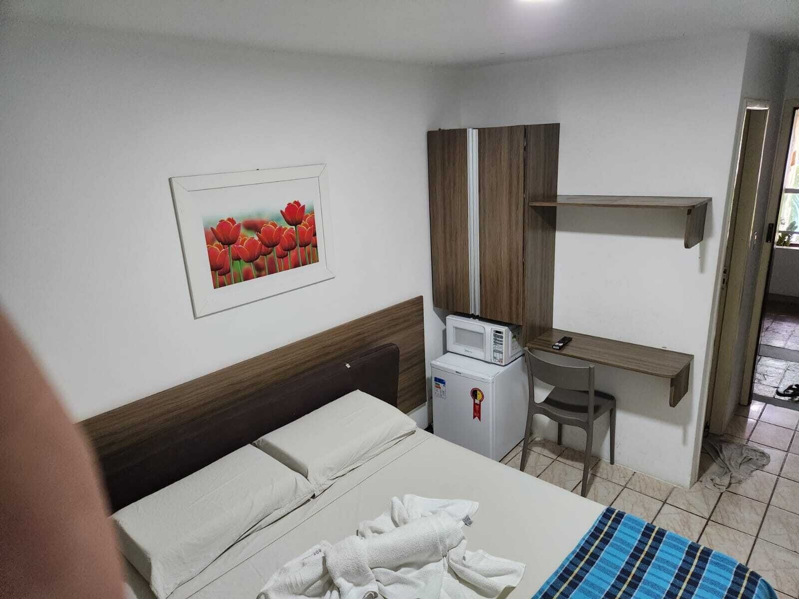 A hotel room with a bed, a desk, a microwave, and a refrigerator.