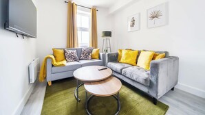 A living room with two grey sofas, yellow cushions, a round wooden coffee table, and a floor lamp. - Central Apartment | Contractors & Families | WiFi (Aldershot)