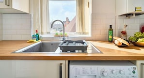 A kitchen with a stainless steel sink, a dish rack, a bottle of olive oil, and a bottle of dish soap.