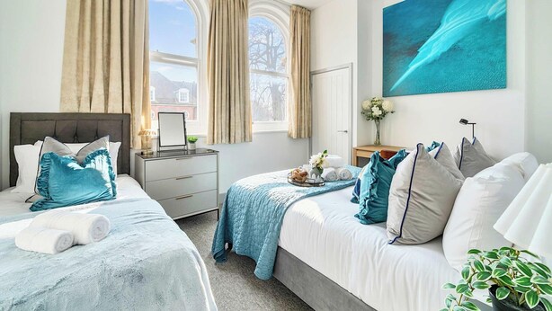 A hotel room with two beds, a large window with curtains, a painting, a bedside table with a lamp, and a potted plant. - 1 Bed 1 Bath Apt, Contractors & Families, Parking (North Camp)