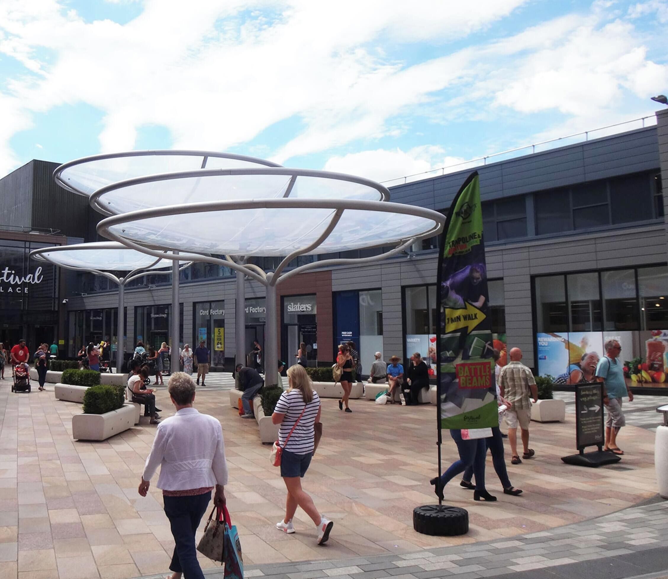 A public square with a modern building featuring a glass facade and a large, circular, transparent canopy structure.
