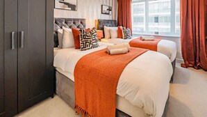 Une chambre d’hôtel avec deux lits, une armoire sombre, une fenêtre avec des rideaux et un radiateur.