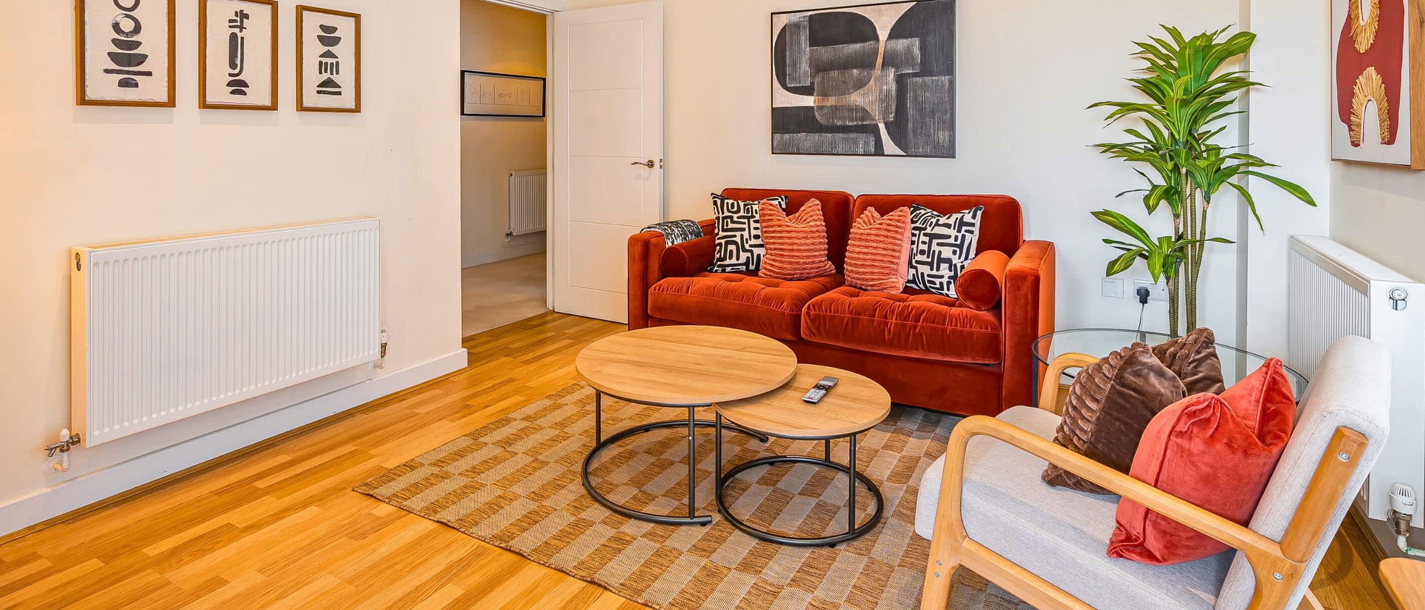 Un salon chaleureux avec un canapé rouge, deux petites tables rondes en bois, un tapis à motifs et une plante en pot.