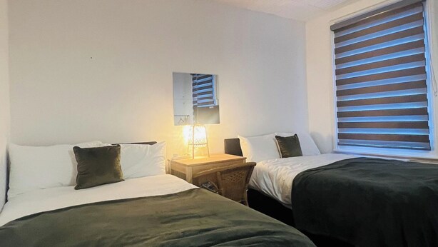 Une chambre d’hôtel avec deux lits, une table de chevet, une lampe, un miroir et une fenêtre avec des stores.