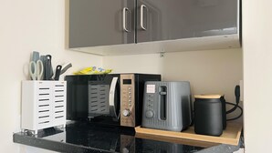 Une cuisine équipée d’un four à micro-ondes, d’un grille-pain et d’une machine à café, le tout posé sur un plan de travail noir.