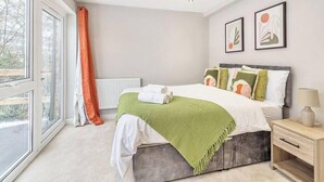 Une chambre à coucher avec un lit, une table de chevet, une fenêtre avec des rideaux et deux tableaux encadrés accrochés au mur.
