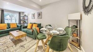 Un salon moderne avec un canapé vert, une table à manger en verre et une bibliothèque.