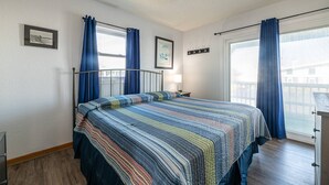 A bedroom with a bed, a nightstand, a ceiling fan, and a window with curtains. - Southern Comfort - KDH MP 7.5, Semi-Oceanfront, 140 Yds to Beach, Hot Tub, Pets OK, Flex Stays (Kill Devil Hills)