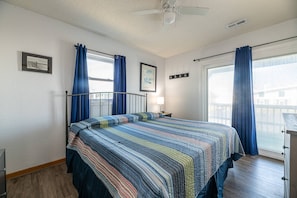 A bedroom with a bed, a nightstand, a ceiling fan, and a window with curtains. - Southern Comfort - KDH MP 7.5, Semi-Oceanfront, 140 Yds to Beach, Hot Tub, Pets OK, Flex Stays (Kill Devil Hills)