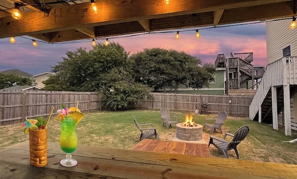A backyard with a wooden deck, outdoor seating, a fire pit, and a wooden fence.