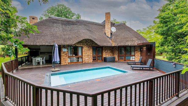Een rieten huis met een zwembad, houten terras en een zitgedeelte buiten.