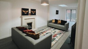 A living room with a fireplace, a sofa, a patterned rug, and artwork on the wall. - Stunning 3-bed House in Oldbury (Oldbury)
