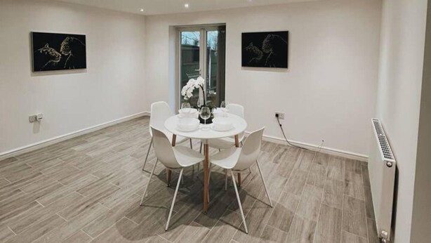 A dining area with a round table, white chairs, and two black-framed paintings on the walls. - Stunning 3-bed House in Oldbury (Oldbury)