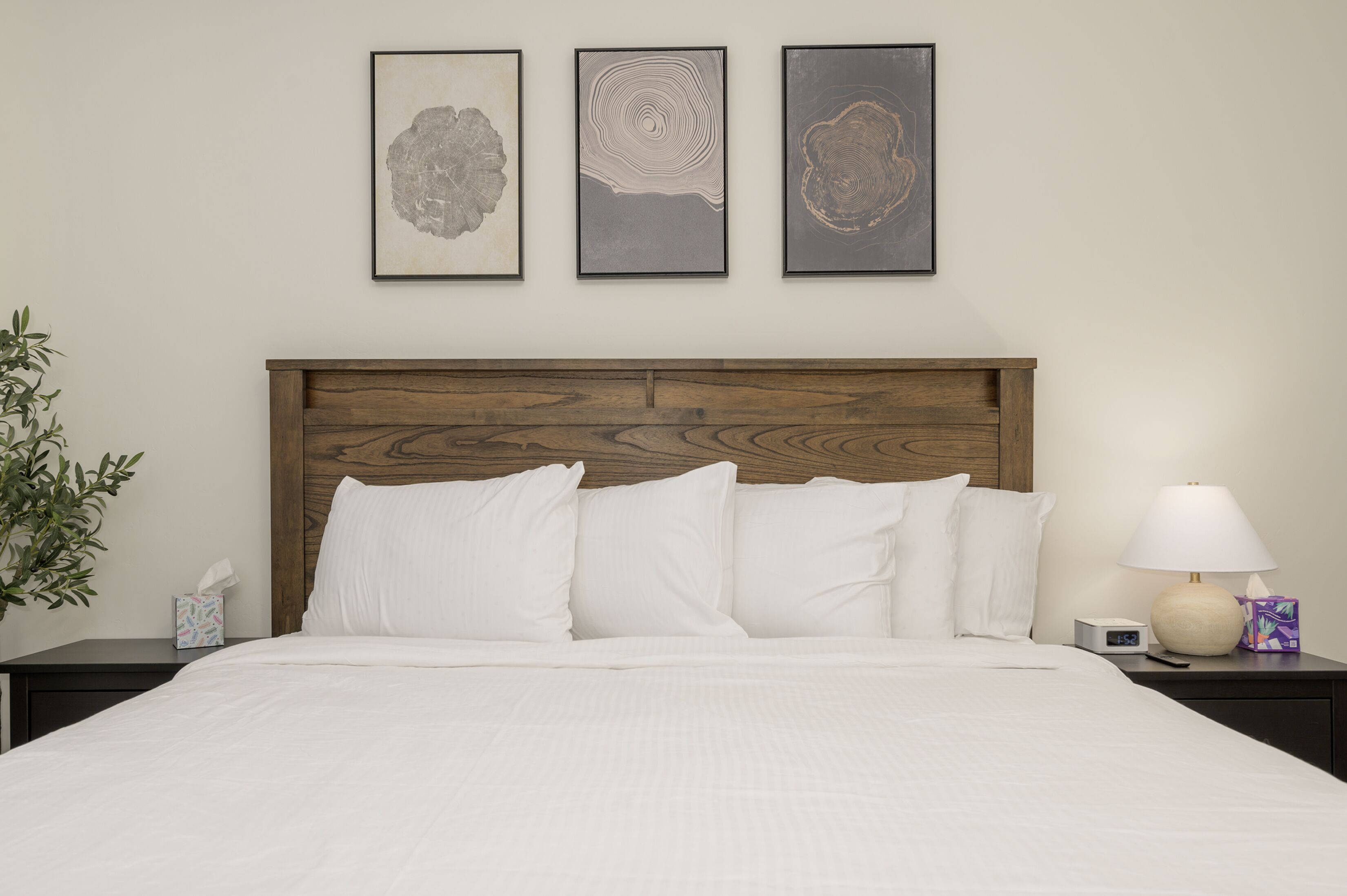 A neatly made bed with white linens, a wooden headboard, and three framed artworks above it.