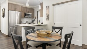 Una cocina moderna con electrodomésticos de acero inoxidable, una mesa de comedor de madera con sillas y una puerta blanca al fondo.