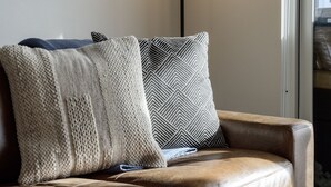 Un sofá de cuero marrón con dos almohadones, uno tejido y otro con diseño en zigzag.