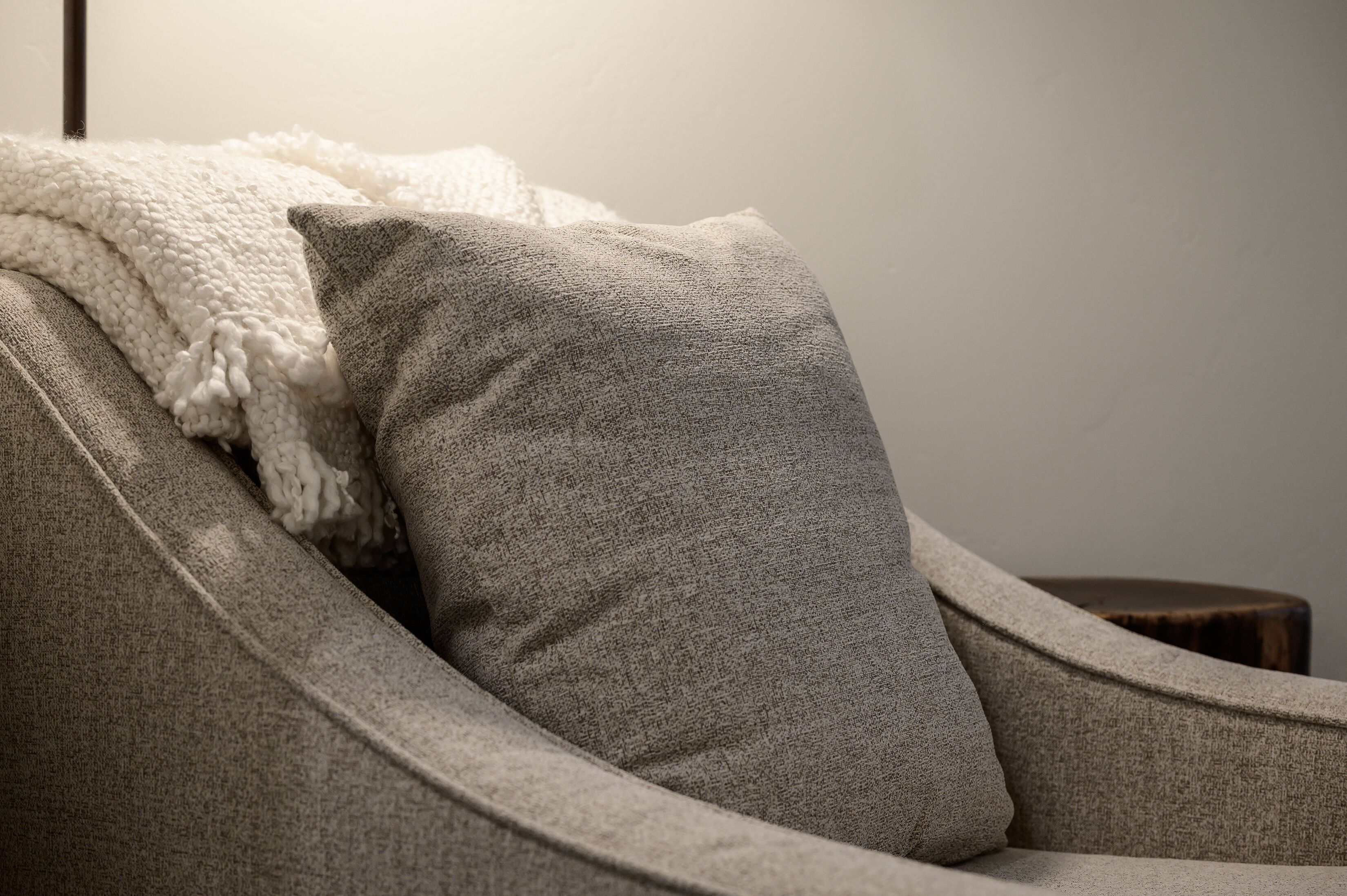 A grey upholstered armchair with a white knitted throw blanket.