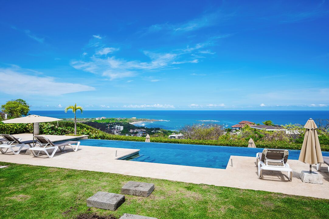 A pool with a view of the ocean, lounge chairs, and umbrellas.