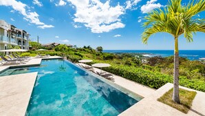 Une piscine entourée de verdure, dotée de chaises longues et de parasols, et offrant une vue imprenable sur la côte.